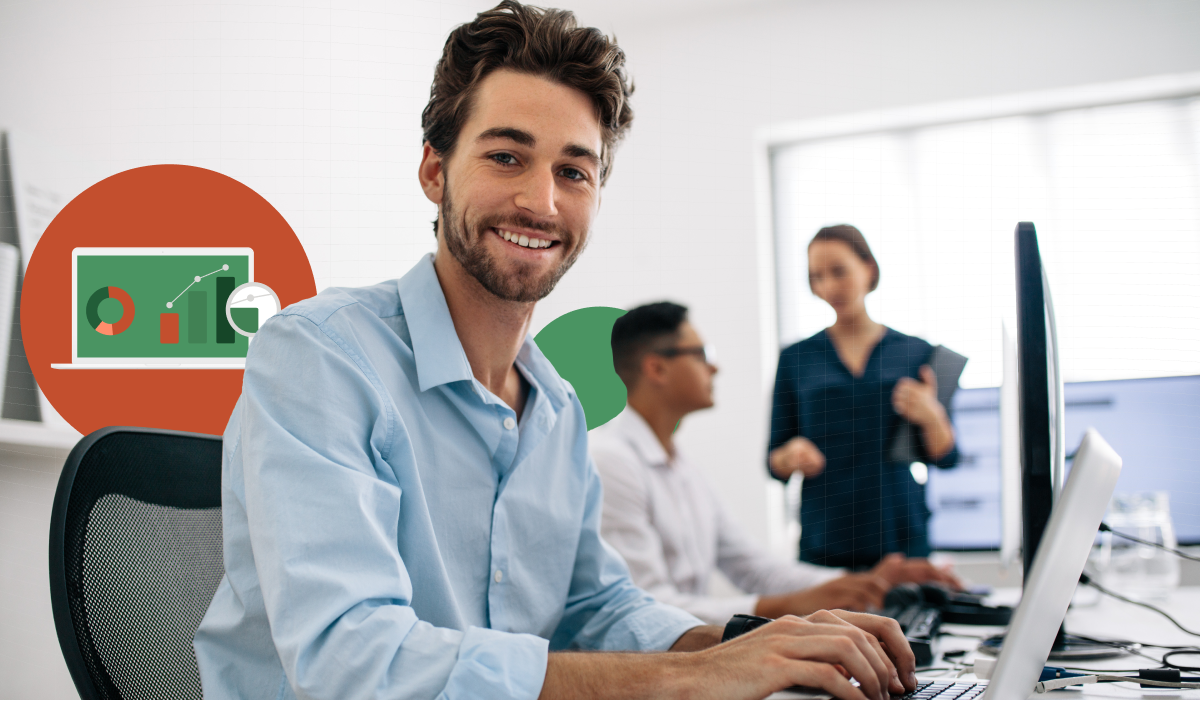 A man sat at a desk with his laptop, smiling towards the camera.