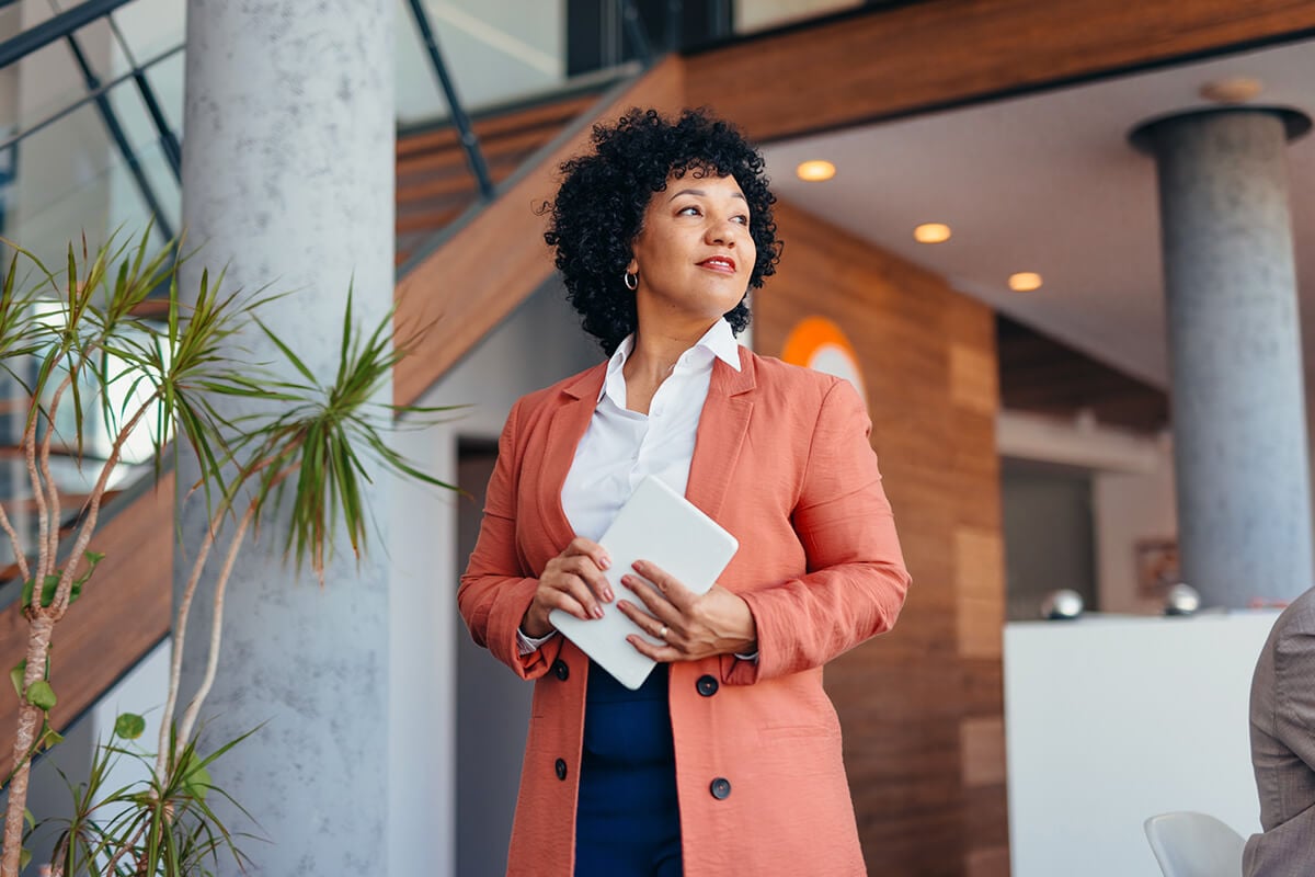 A professional woman in a suit holds a tablet, appearing focused and engaged in her work.
