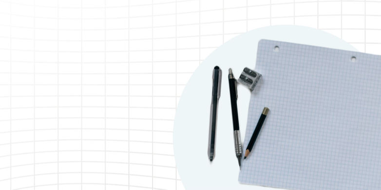 Pens, a pencil, and a small sharpener on top of grid paper.