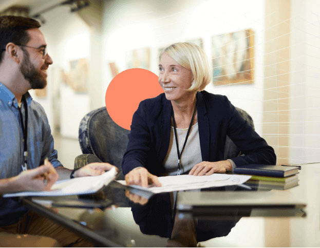 A woman and man smiling at each other while sitting at a table with papers on it.