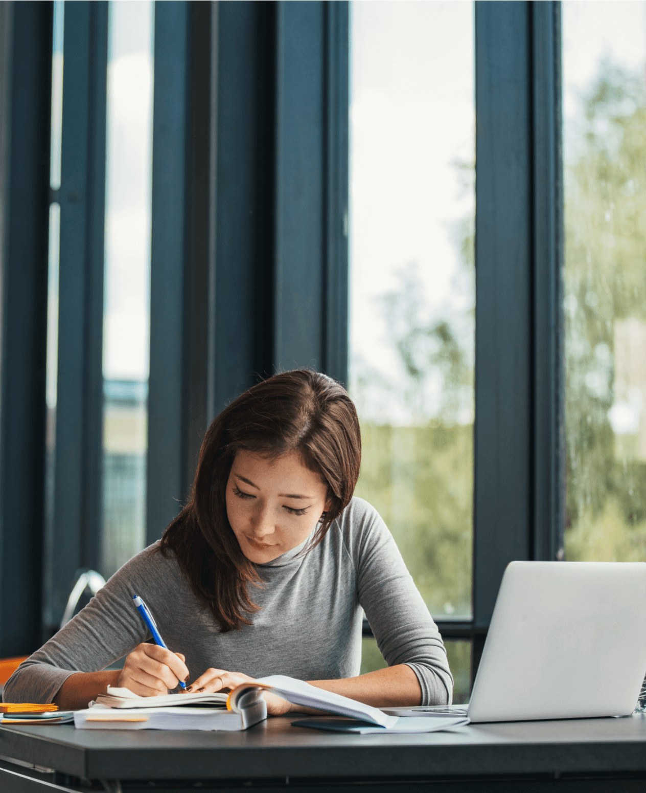 Photo of young Asian female student sitting at table and writing on notebook. Young female student studying in library.