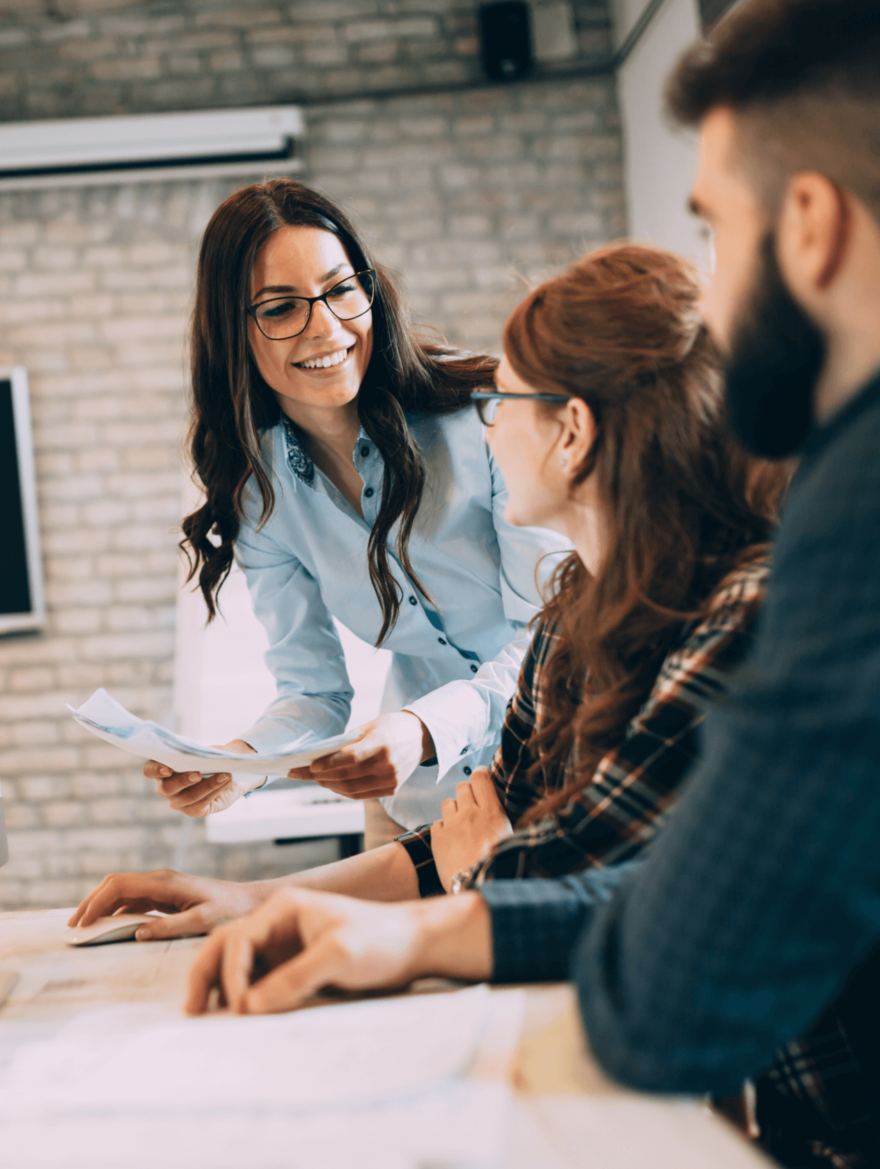 Female business leader speaking to a group of colleagues at a desk.