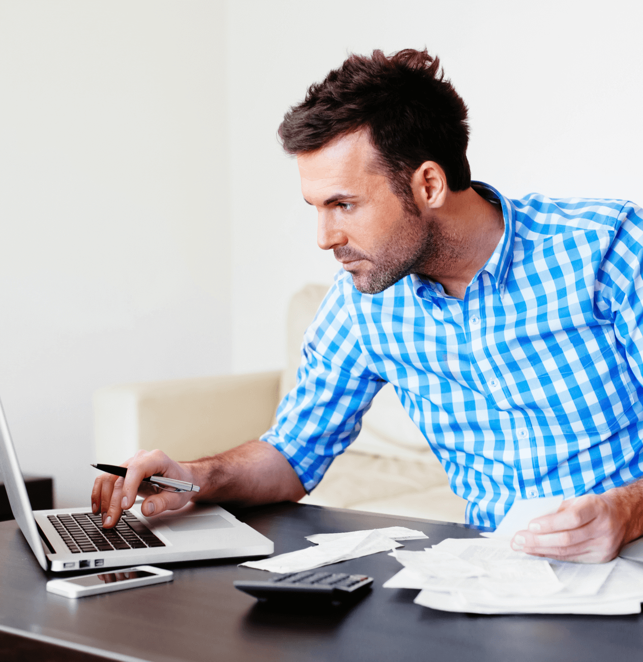 Caucasian man in a blue checkered shirt working on a laptop computer.
