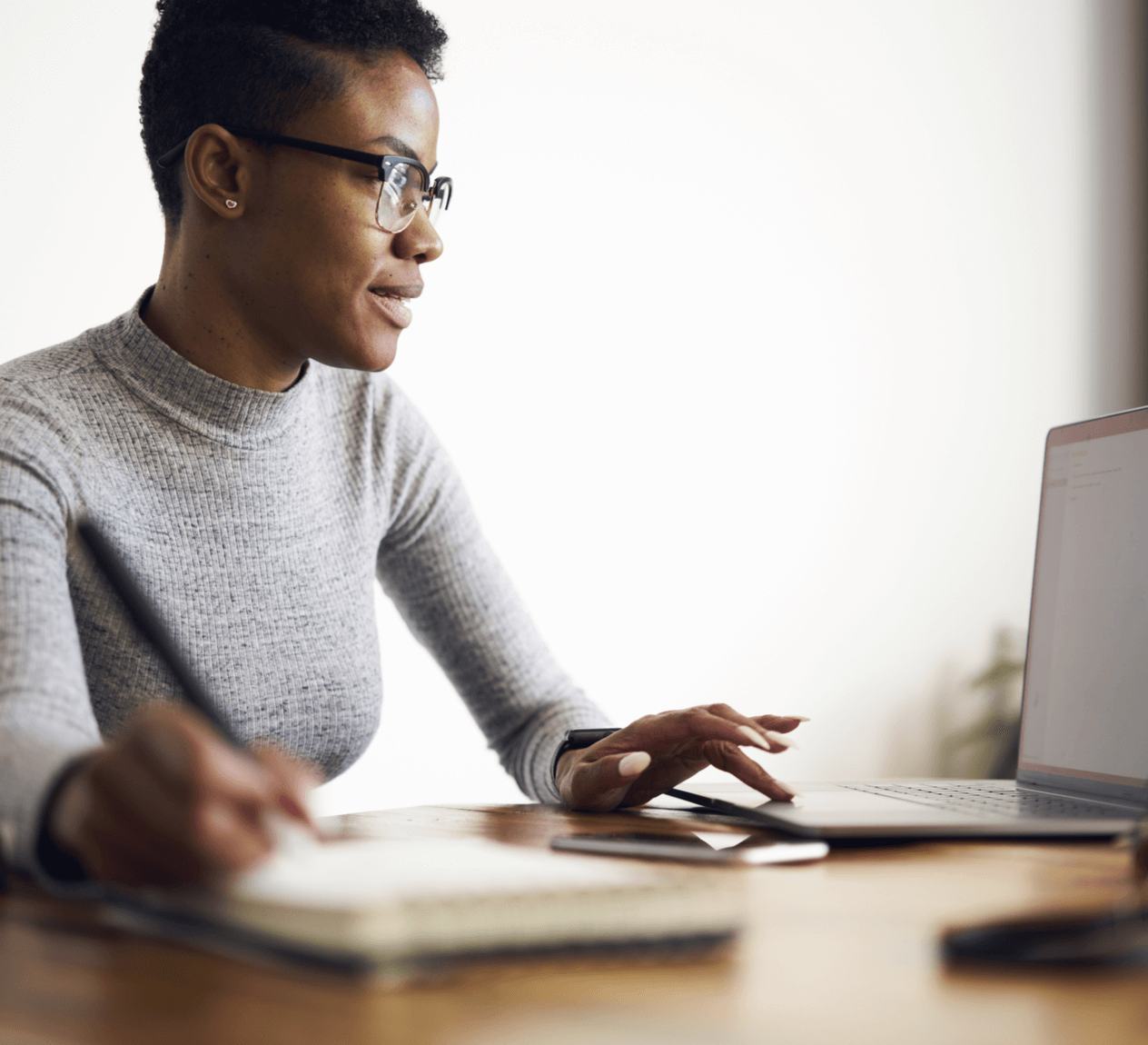 African American woman with short hair and glasses working on a laptop computer.