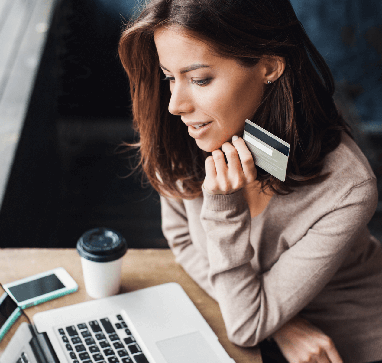 Caucasian woman with brown hair holding a credit card while looking at a laptop computer.