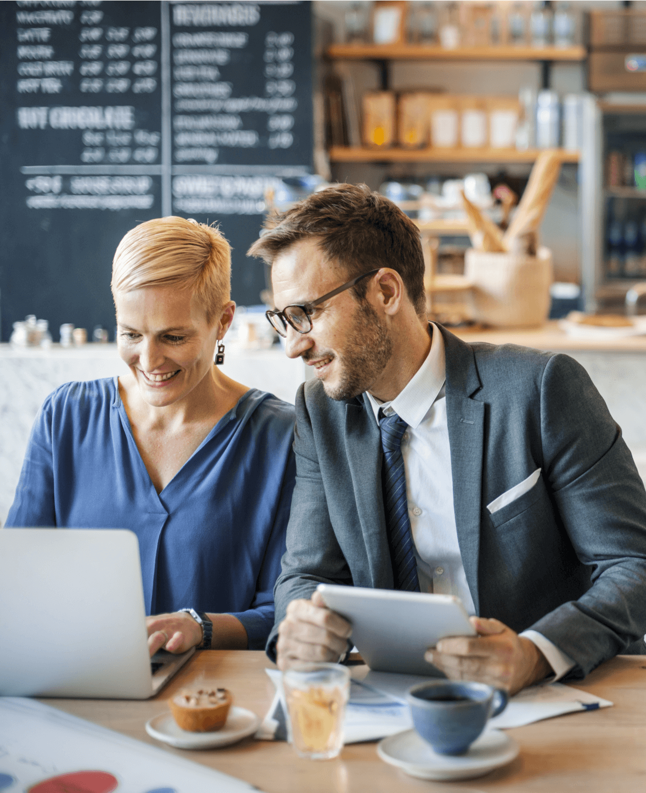 A woman and a man wearing business clothes working together on a laptop computer in a cafe.