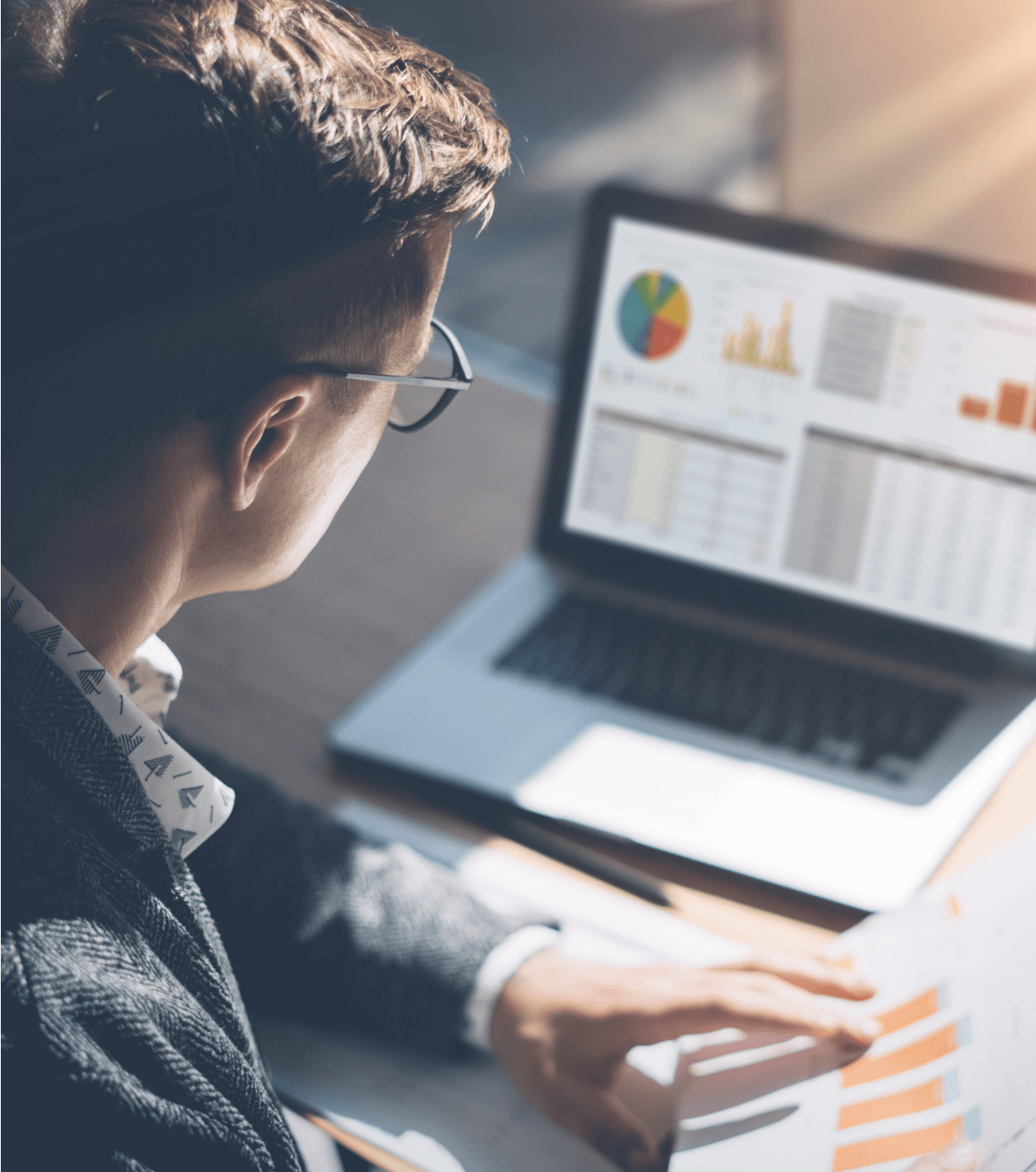 Man looking at laptop and holding papers with graphs.