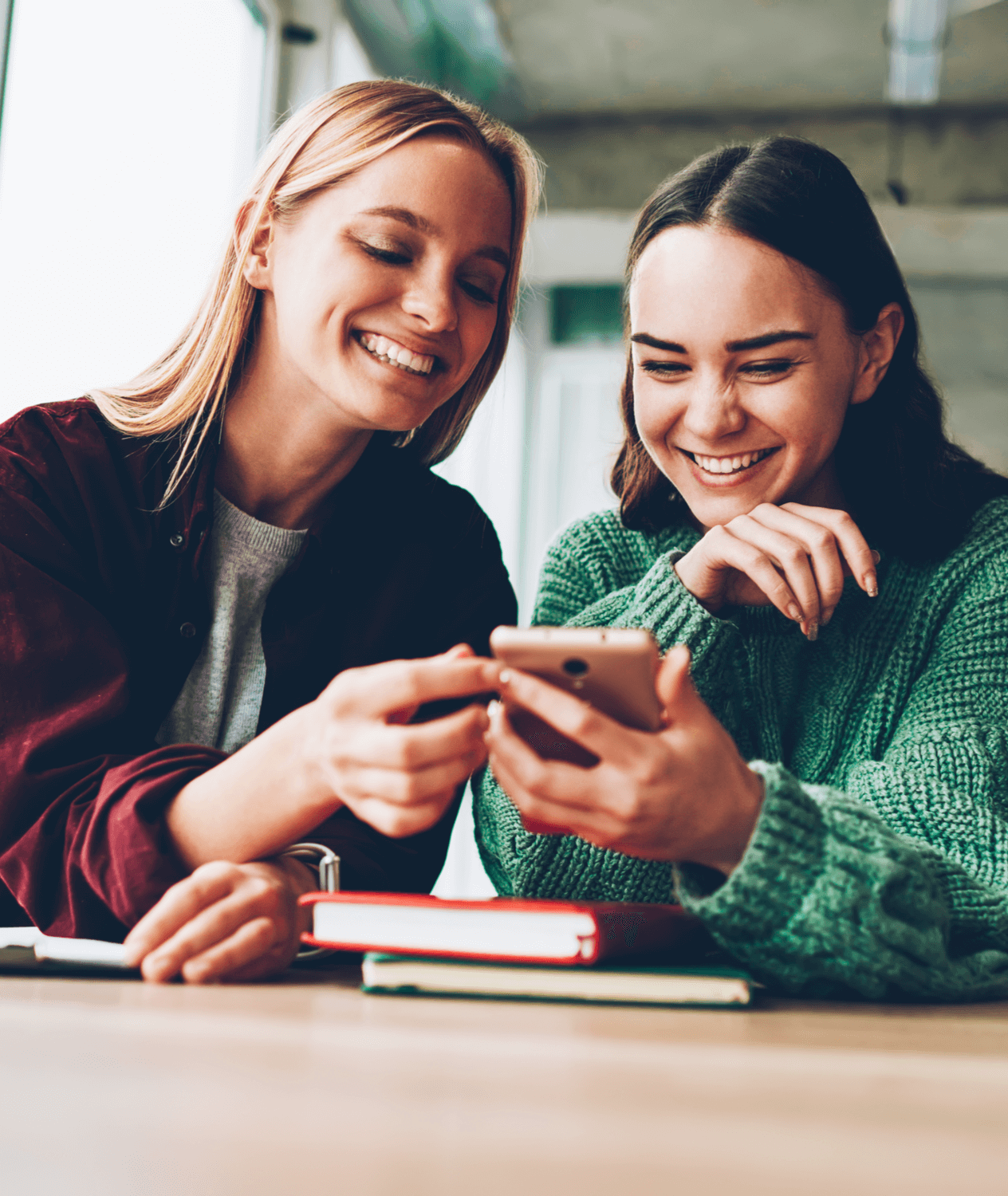 Two Caucasian women smile while looking at a cell phone.