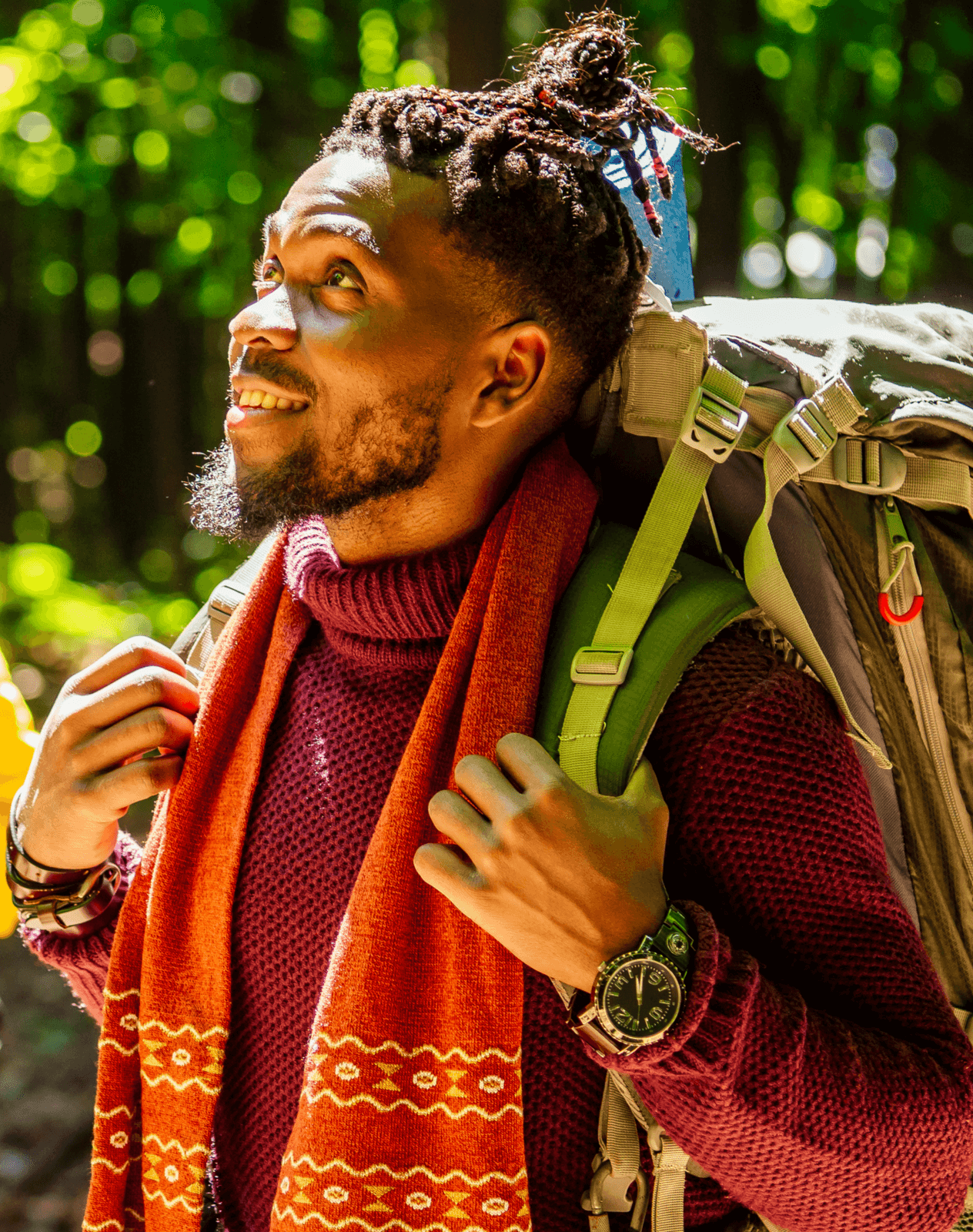 Black man hiking through the forest while looking up at the trees.