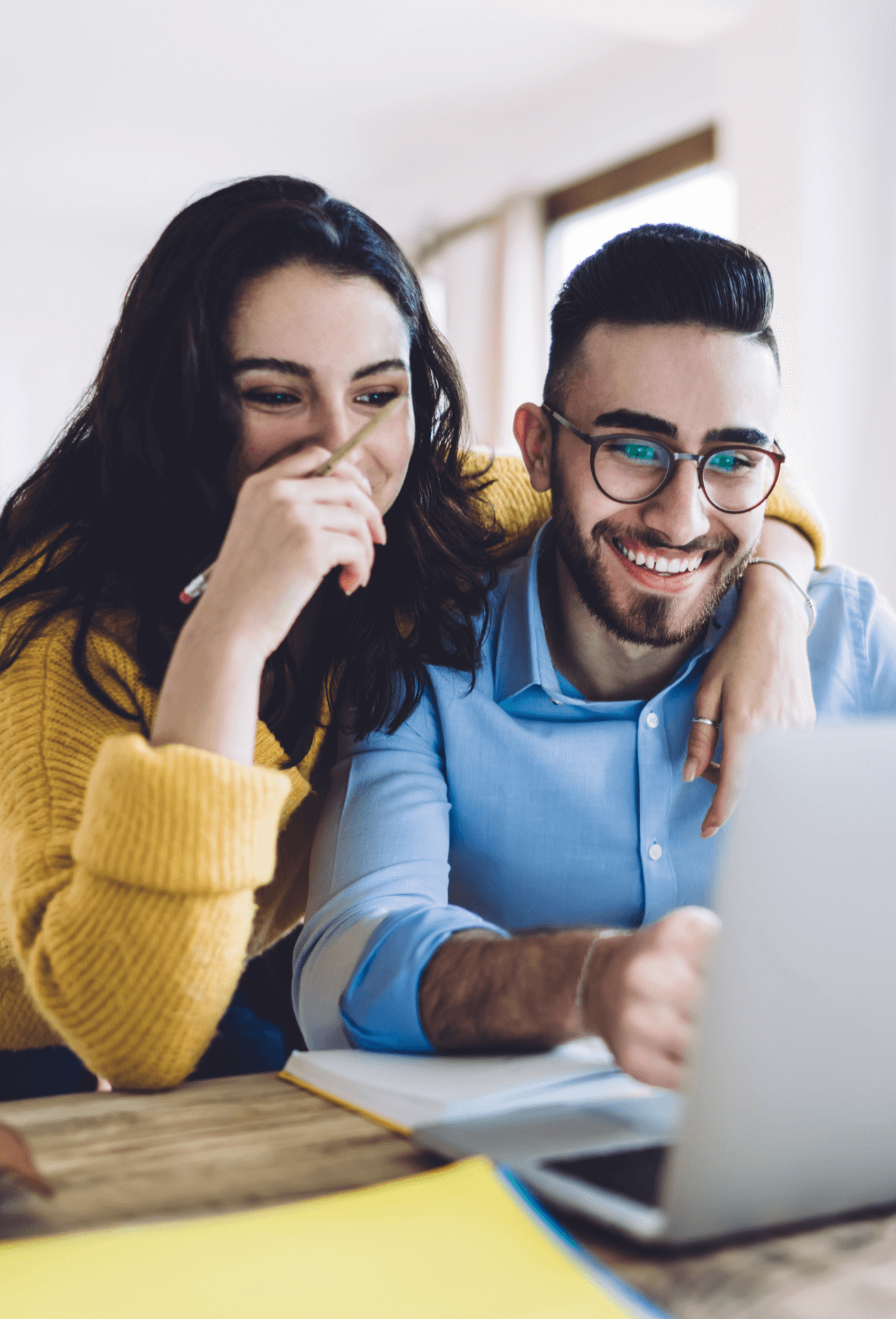 A man and a woman sitting at a desk, smiling at a laptop.