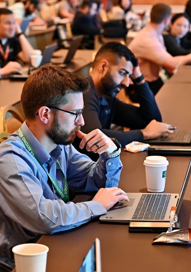 People seated at a conference table working on laptops, with coffee cups and snacks nearby.