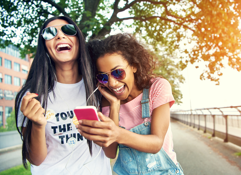 Image of two woman outside walking, laughing and listening to music