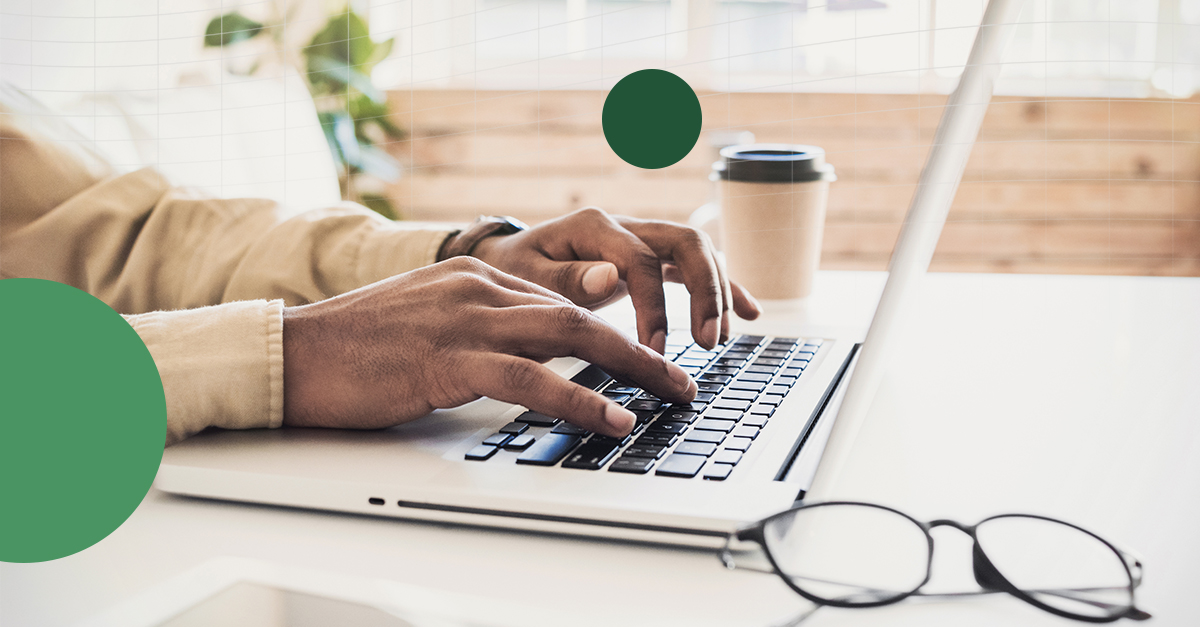 Pair of man's hands typing on laptop. Coffee cup and glasses on table.