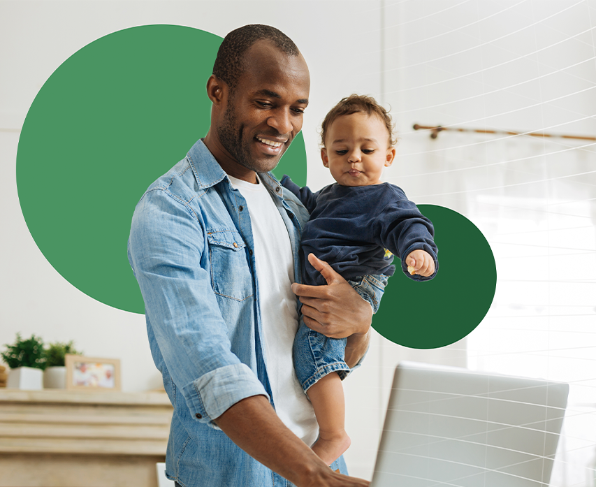 Man holding baby and typing on laptop