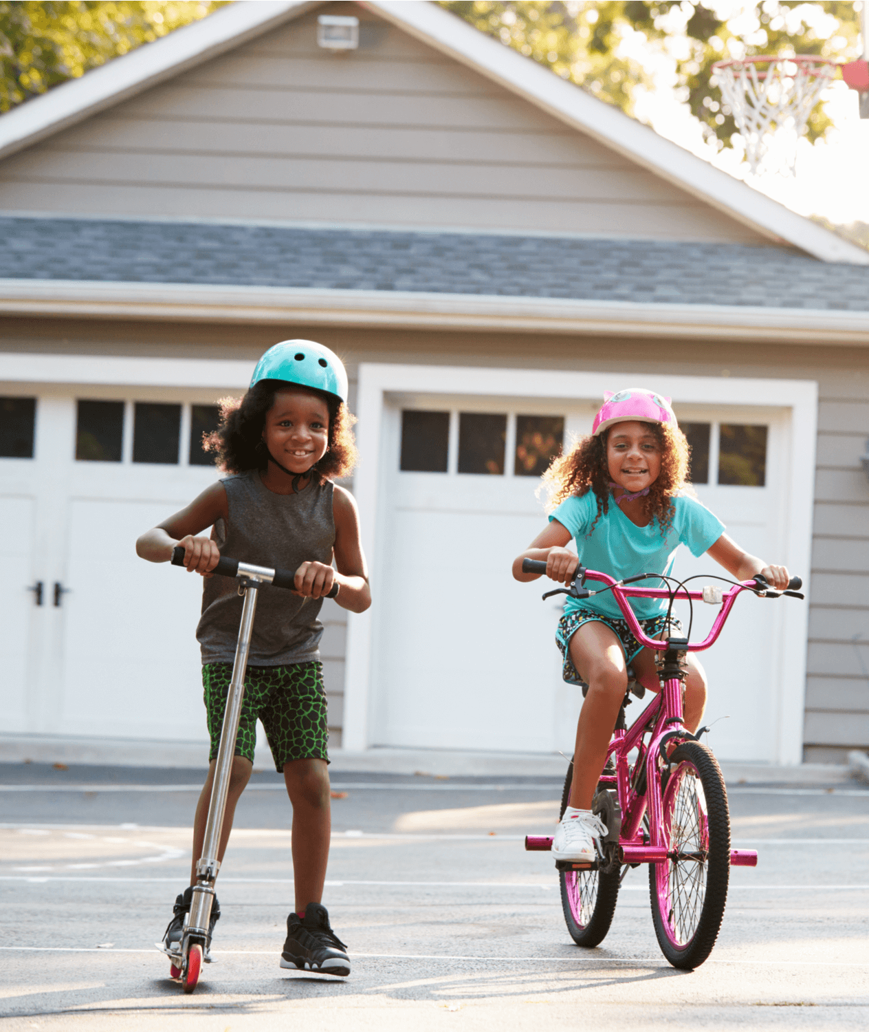 Portrait of two young African American girls. One is riding a scooter and the other is riding a bike.